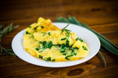 Tahta bir tabakta doğranmış yeşil soğanlı kızarmış omlet.