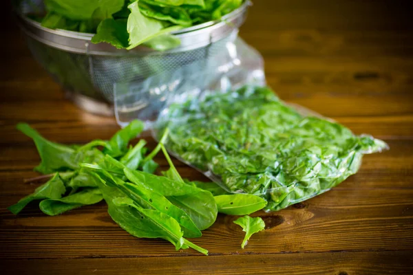 Fresh green sorrel in a vacuum bag, in a colander on a wooden table — Stock Image Fresh Green Sorrel Vacuum Bag Colander Wooden Table Stock Photo