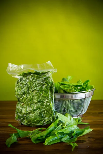 Fresh green sorrel in a vacuum bag, in a colander on a wooden table — Stock Image Fresh Green Sorrel Vacuum Bag Colander Wooden Table Royalty Free Stock Images