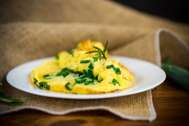 Tahta bir tabakta doğranmış yeşil soğanlı kızarmış omlet.