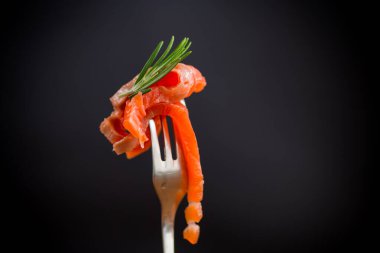 Çatallı, siyah arka planda tuzlu kırmızı balık dilimi.