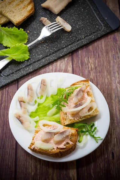 Бутерброд с салатом, сельдь и травы с луком в тарелке — стоковое фото