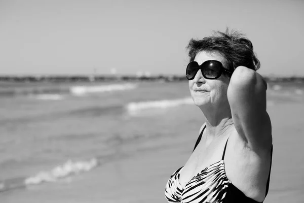 Senior mulher de pé na praia — Fotografia de Stock