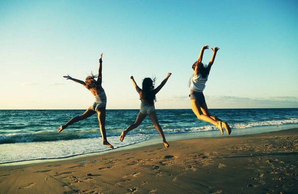 Three girlfriends jumping on the beach  