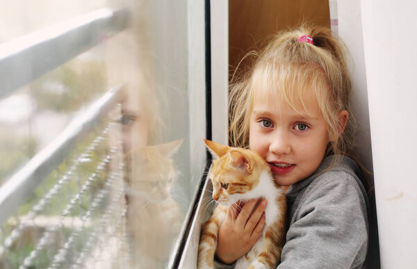 Portrait of a adorable little girl with kitten near the window