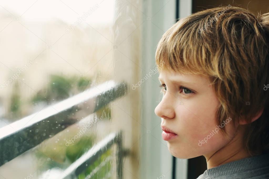 Cute 10 years old autistic boy looking through the window