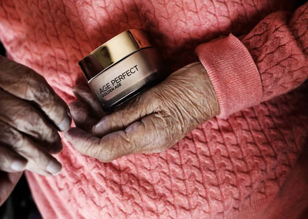 Mulher idosa segurando uma caixa de creme com a inscrição: dourado y — Fotografia de Stock