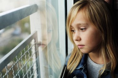 Bir Windo 'nun yanında oturan 9 yaşındaki üzgün bir kızın portresi.