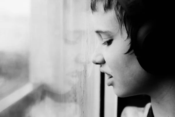 Teenage 12 years old boy looking through the window on the rain — Stock Photo, Image