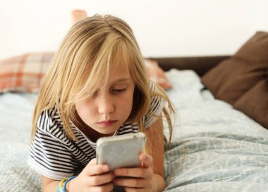 Covid-19. Ev okulu konsepti. 9 yaşındaki bir kız evde cep telefonuyla sıkılıyor..