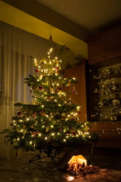 Krippendekoration unter beleuchtetem Weihnachtsbaum Stockfoto