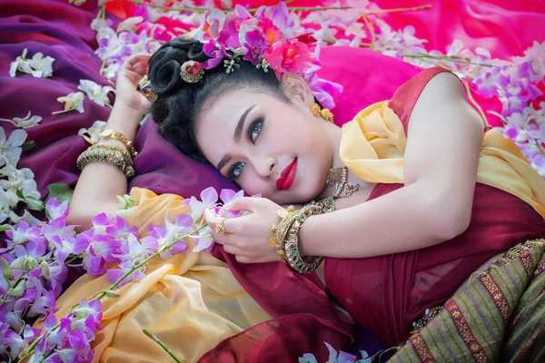 Thailändische Frau trägt typisches thailändisches Kleid mit Blumenhintergrund, — Stockfoto