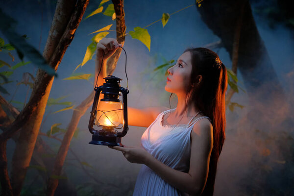 Woman with Vintage Lantern Outside at Night - Cosplay girl in nutral costume holding a lamp, Young woman in white long dress walking in night wood
