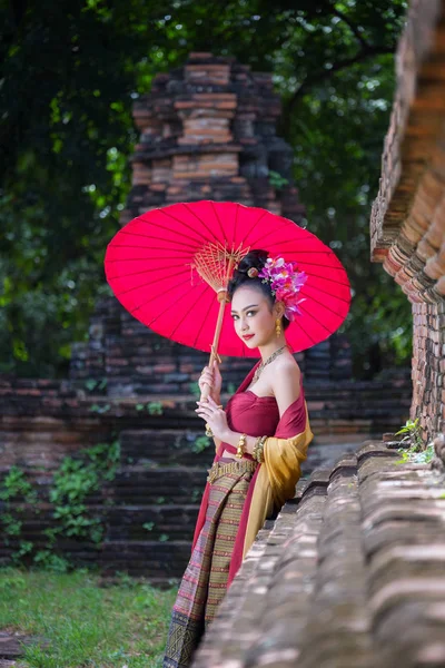 Schöne thailändische Mädchen in traditioneller Kleidung Kostüm roten Regenschirm als — Stockfoto