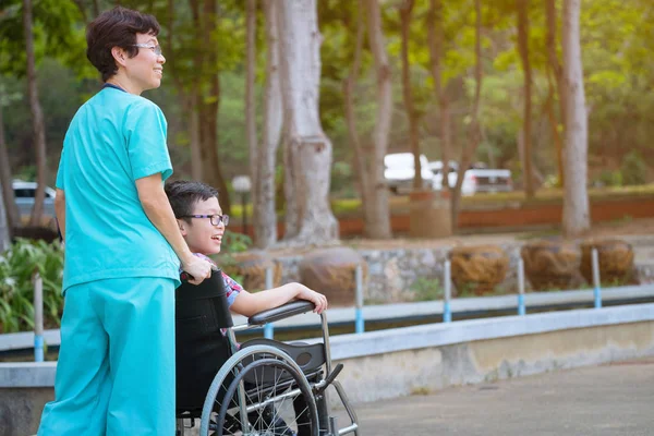 Glimlachend verzorger Senior verpleegkundige zorg de patiënt van een jongen in de wheelc — Stockfoto
