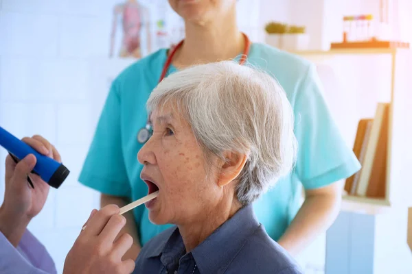 Arzt untersucht Hals der Seniorin mit Taschenlampe — Stockfoto