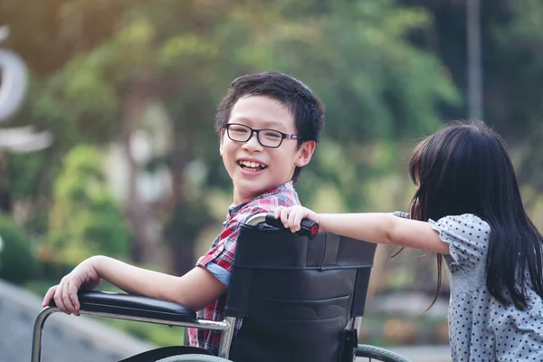 Niño feliz en silla de ruedas con chica tratar de conducir una silla de ruedas de su — Foto de Stock