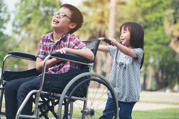 Heureux garçon en fauteuil roulant avec fille essayer conduire un fauteuil roulant de son — Photo