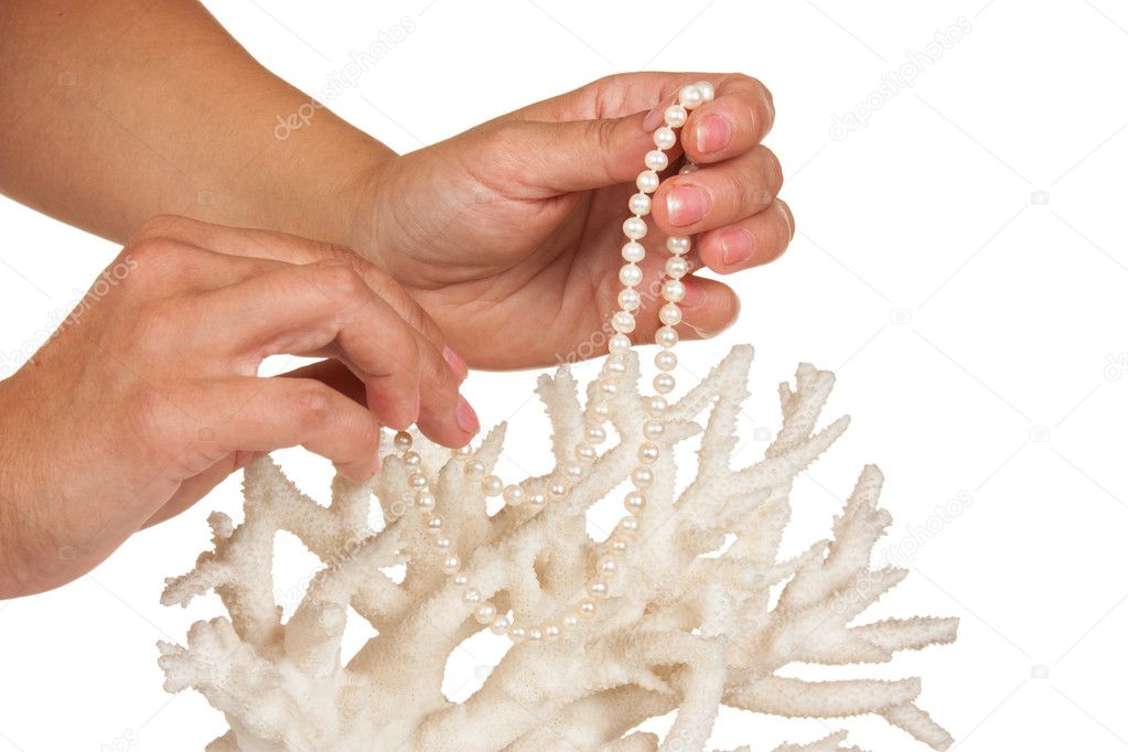 a pearl necklace in woman hands against the backdrop of coral isolated on a white background