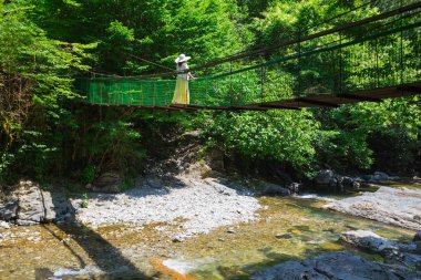 Şapkalı Kız bir asma köprü çalılıkları ormanın içinde bir fırtınalı dağ nehir üzerinde elini kolunu sallaya dönüyor