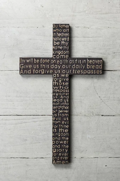 Wooden cross with carved the Lords Prayer on white worn wooden background