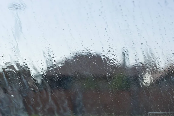 Water drop on glass outside the window, houses background.