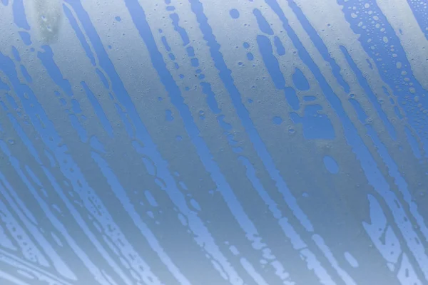 Soap detergent foam on a clear glass. Blue background. — Stock Photo, Image
