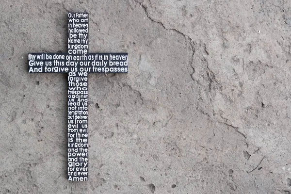 Wooden cross with the Lord\'s prayer on the grey concrete with cracks background.