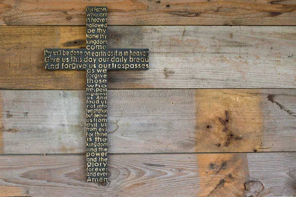 Černý dřevěný kříž se Otčenáš na pozadí omšelé dřevěné prkno. — Stock fotografie