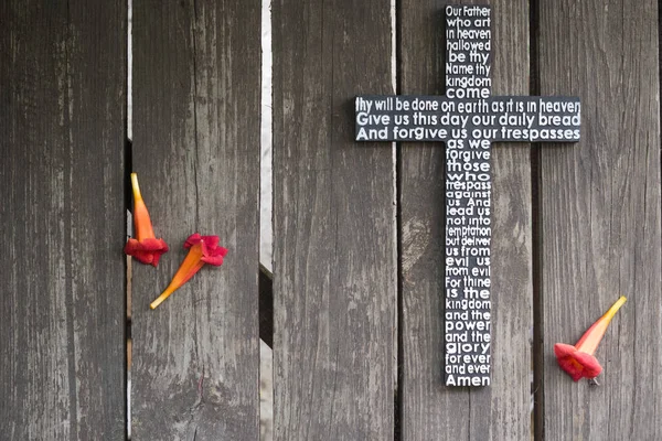 Wooden cross with the Lord\'s prayer  on the shabby wooden  plank with red flowers.