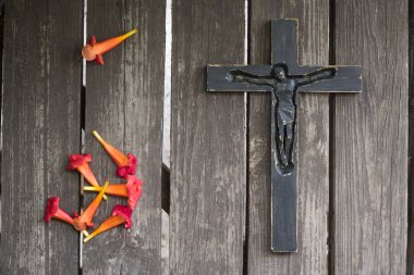 Kırmızı çiçekli eski püskü ahşap tahta üzerinde siyah tahta haç.