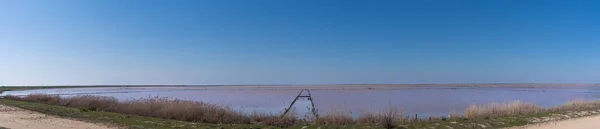 Lago salado rosado con un viejo muelle de madera. Un antiguo método de extracción de sal del mar . — Foto de Stock