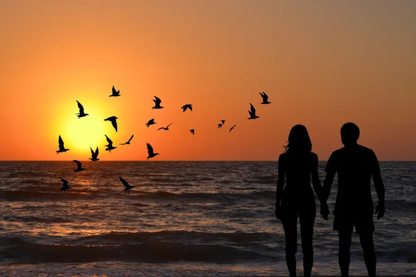 Couple silhouettes holding hands looking at sunrise on the beach — Stock Photo, Image