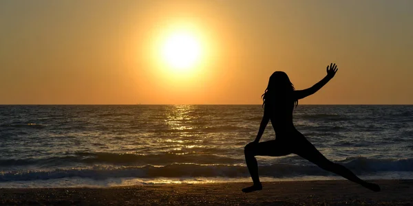 Kadın siluet gündoğumu, sahilde bir yoga poz — Stok fotoğraf