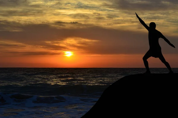 Silhueta homem em uma pose de ioga na costa ao nascer do sol — Fotografia de Stock