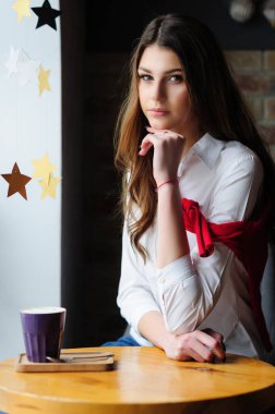 Bir kafede, pencerenin yanındaki masada bir fincan kahveyle oturan kız.