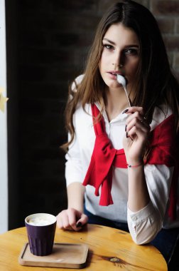 Bir kafede, pencerenin yanındaki masada bir fincan kahveyle oturan kız.