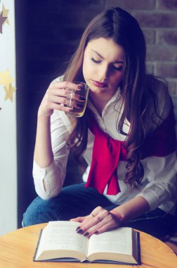 Kafenin penceresinin yanındaki masada bir fincan çay ve bir kitapla bir kız.
