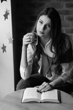 Kafenin penceresinin yanındaki masada bir fincan çay ve bir kitapla bir kız.