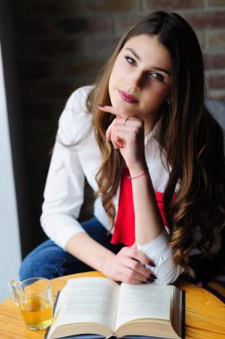 Kafenin penceresinin yanındaki masada bir fincan çay ve bir kitapla bir kız.