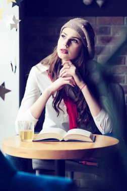 Kafenin penceresinin yanındaki masada bir fincan çay ve bir kitapla bir kız.