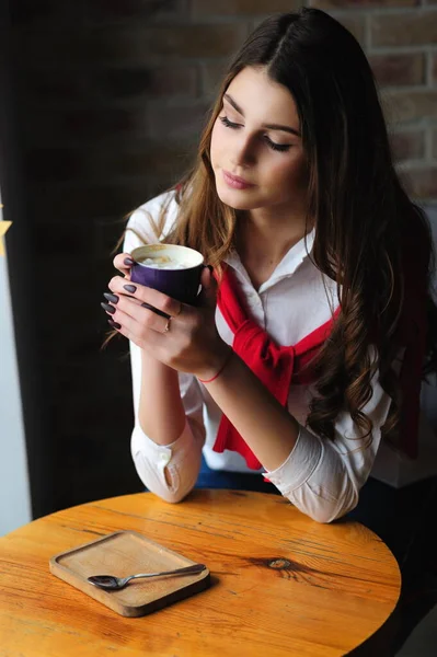 女孩坐在窗边的一张桌子上 在咖啡馆里喝一杯咖啡 — 图库照片