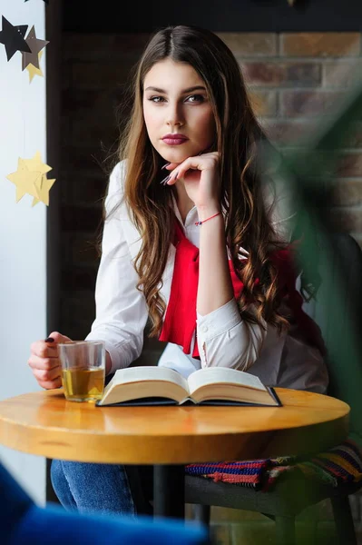 お茶と本が入ったカフェの窓辺のテーブル席の女の子 — ストック写真