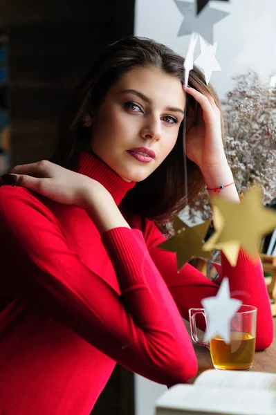 お茶と本が入ったカフェの窓の赤いセーターを着た美しい女の子 — ストック写真