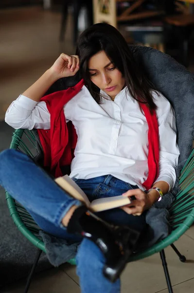 一个穿着白衬衫 坐在椅子上看书的漂亮黑发女孩的画像 — 图库照片