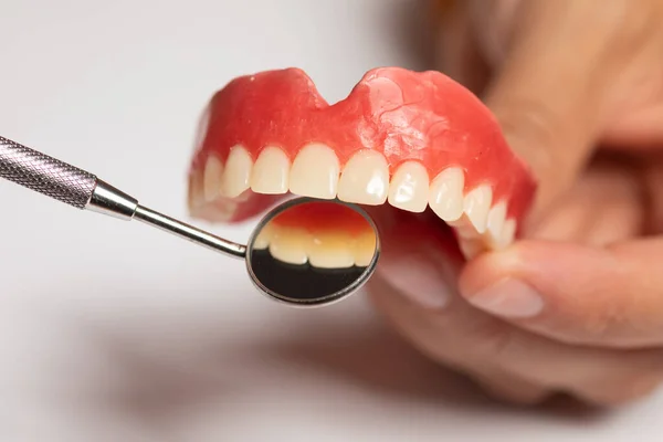 Зубной протез в руках врача-стоматолога, проверка с зеркалом — стоковое фото