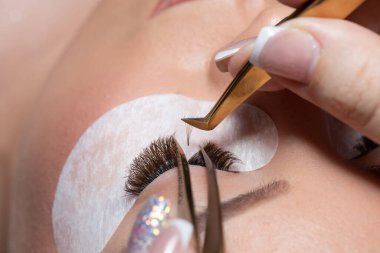 Kirpik uzatma prosedürü. Uzun kirpikli kadın gözü. Kırbaçlar. Cımbızı, makroyu, seçici odağı kapat