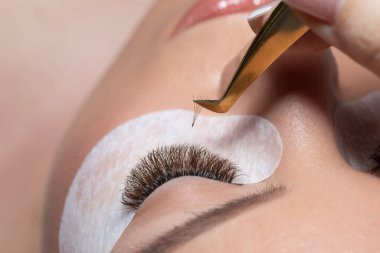 Kirpik uzatma prosedürü. Uzun kirpikli kadın gözü. Kırbaçlar. Cımbızı, makroyu, seçici odağı kapat