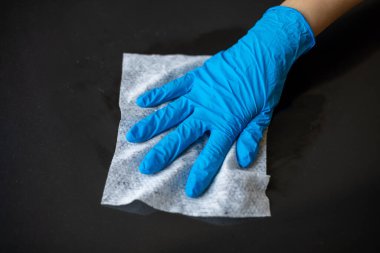 Mavi eldivenli bir kadın ofis masasını ıslak mendille temizliyor.