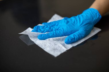 Mavi eldivenli bir kadın ofis masasını ıslak mendille temizliyor.